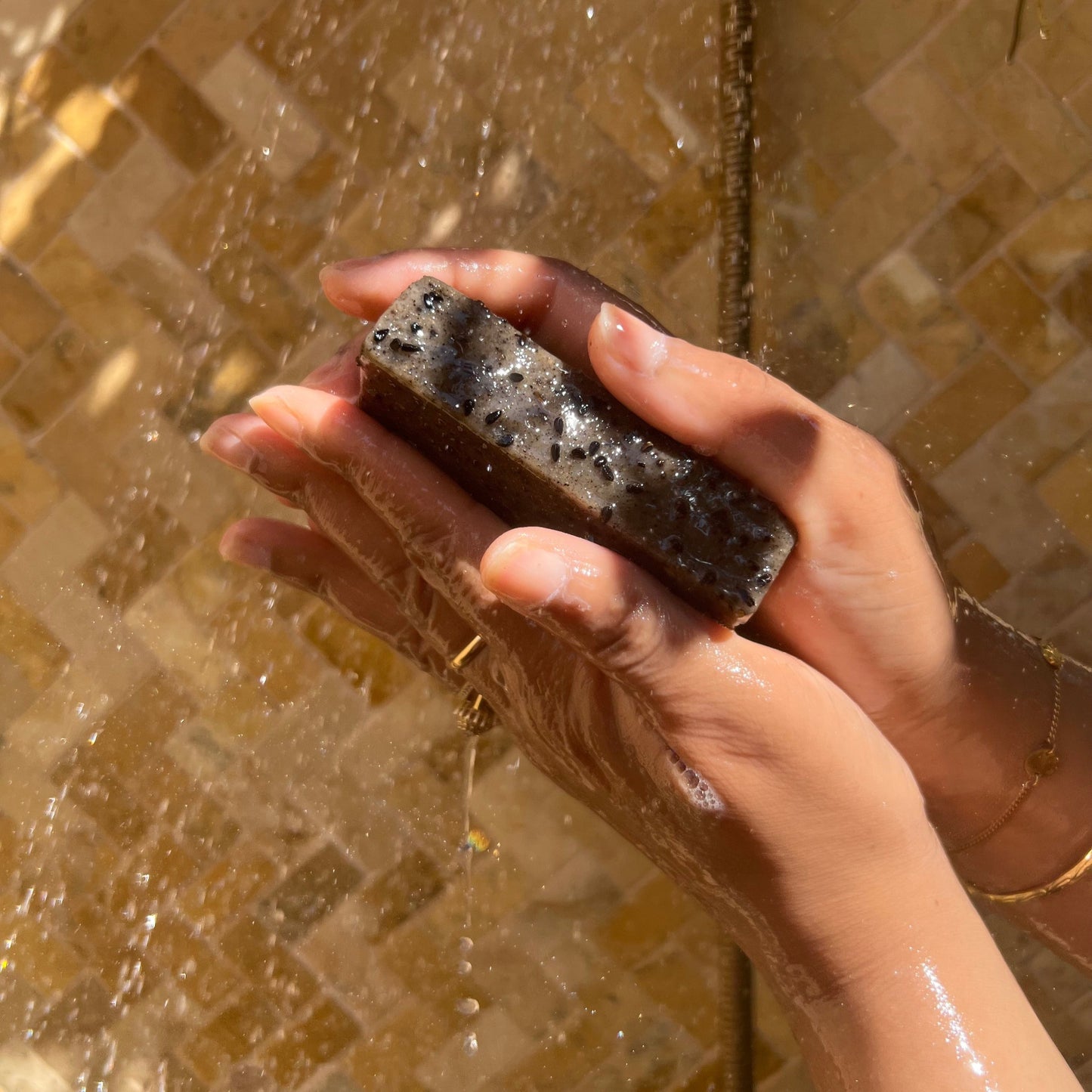 Gros plan sur le savon solide à l'huile de nigelle sous la douche, mettant en évidence les graines de nigelle incrustées dans le savon, illustrant les détails naturels et la texture exfoliante.